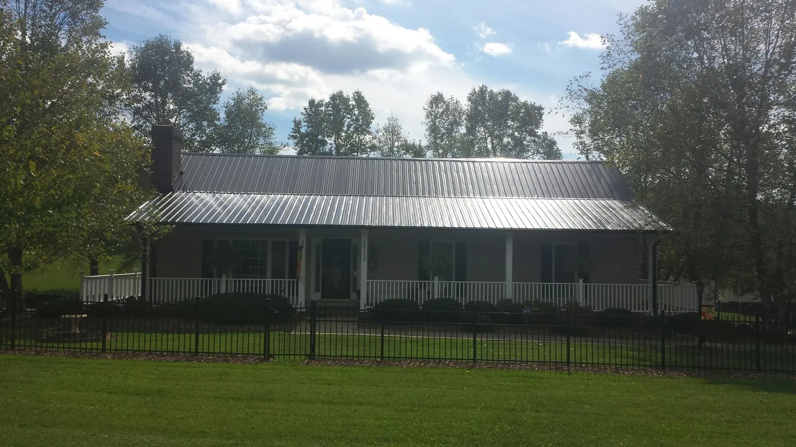 Gray metal roof on a brick ranch with a full width front porch — Gutter Guard Installation work by our crew in Raymond